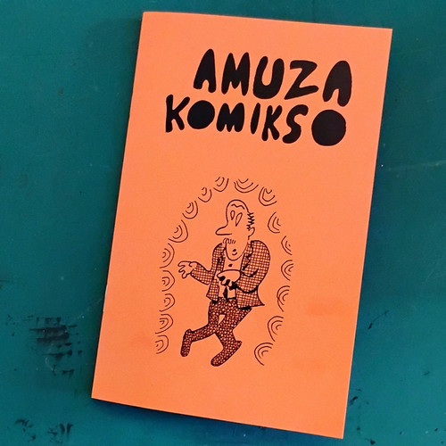 The cover of a digest size comic book called Amuza Komikso (derived form amuse and comics). Funny drawing of a moustached man having a fit surrounded by swirls. 