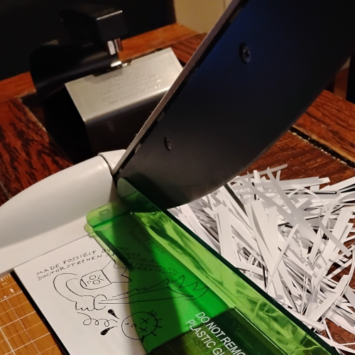 A minicomic in a guillotine trimmer. Slivers of paper in a big pile next to it. 